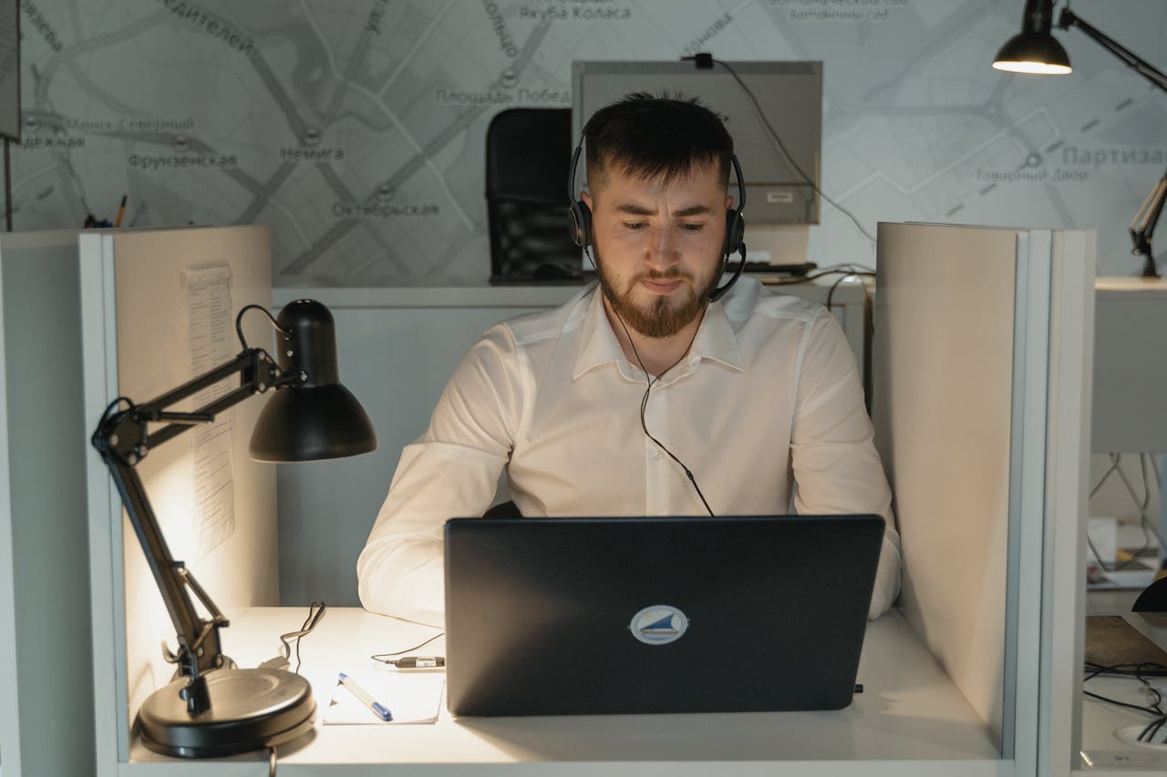 A bearded call center agent wearing headphones, focused on his laptop at work in a modern office.